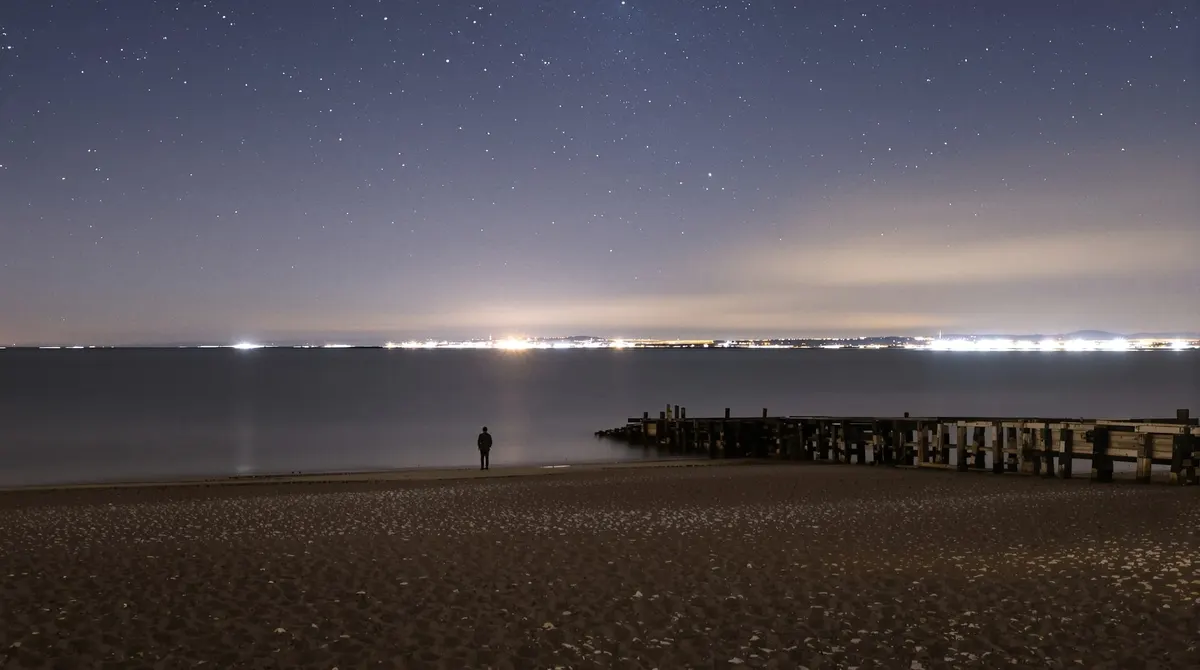 Sternenhimmel über der Elbe am Strand von Övelgönne, eine Person klein von hinten am Wasser