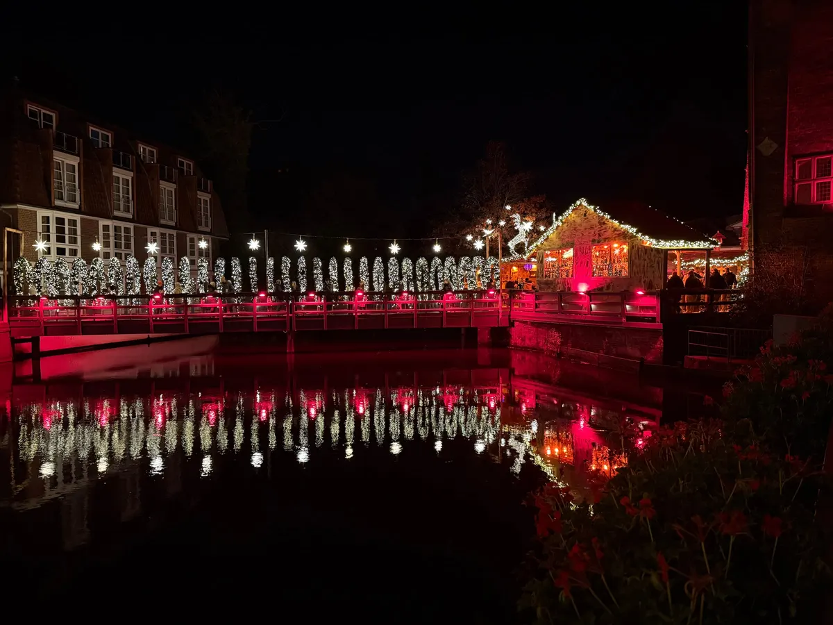 Beleuchtete Holzbrücke mit Lichterbögen und Sternen, Spiegelung im Wasser am Bergström