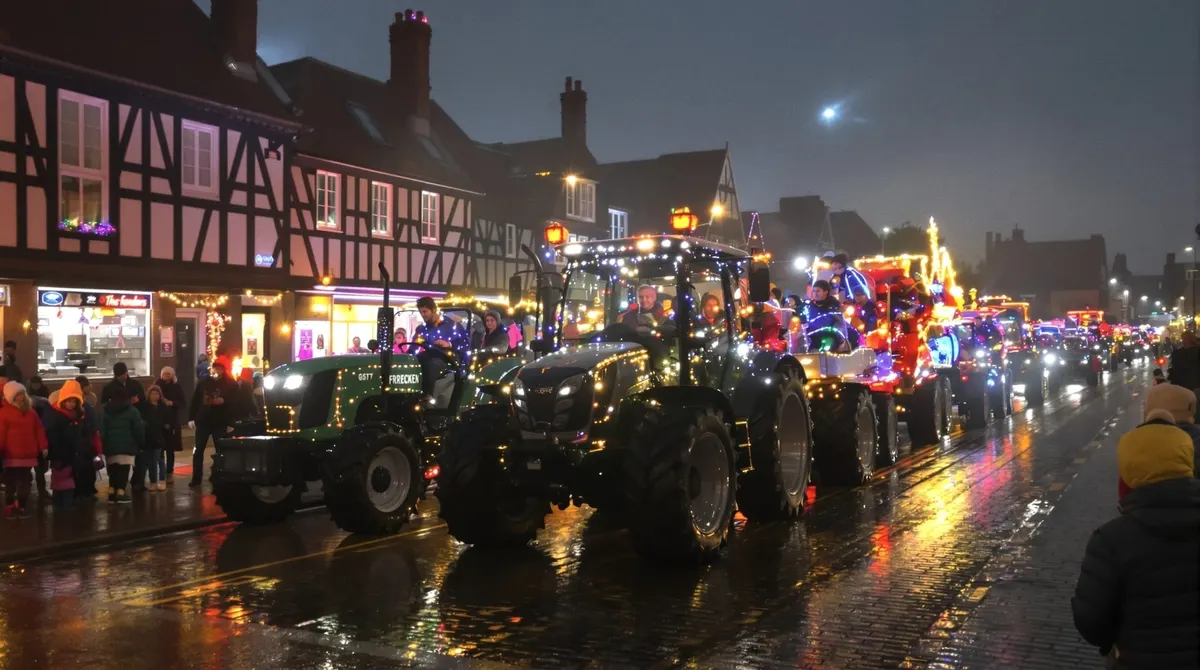 Geschmückte Trecker mit beleuchteten Anhängern fahren abends durch ein Heidedorf mit Fachwerkhäusern