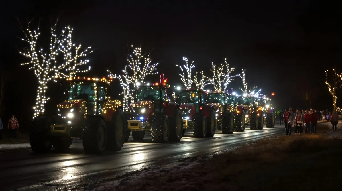 Geschmückte Trecker mit Lichterketten fahren abends über eine Landstraße an der Elbe